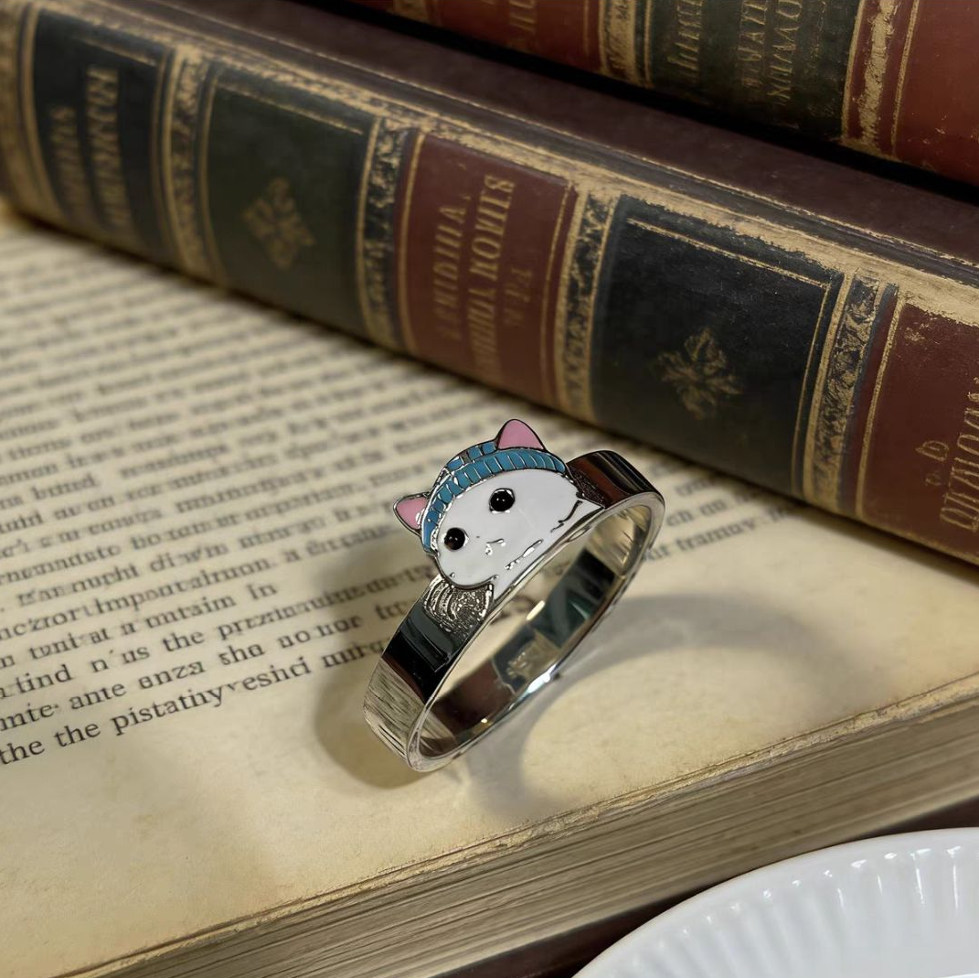 `A 925 sterling silver cat ring featuring a cute cat wearing a blue beanie, resting on top of antique leather-bound books.