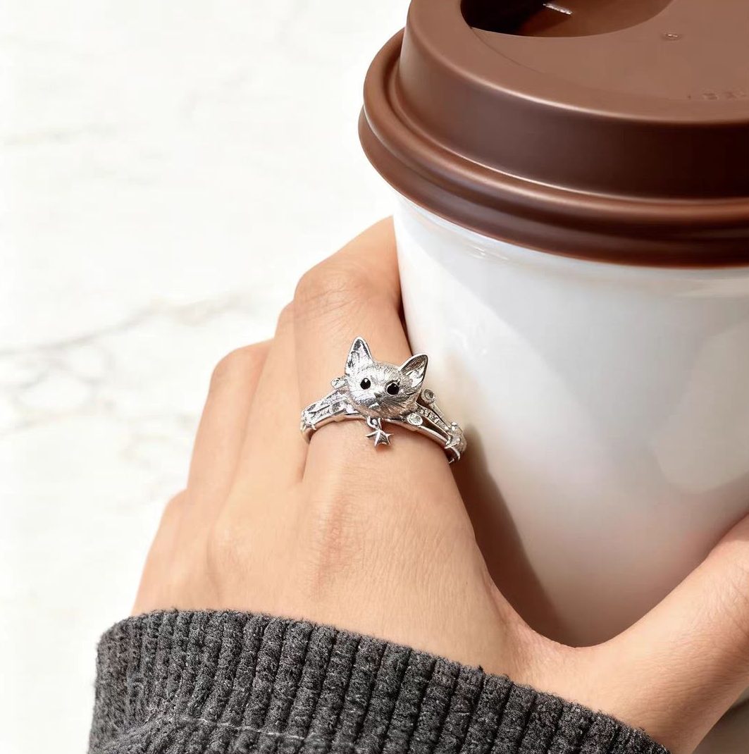 A 925 sterling silver ring with a detailed matte textured cat face, worn on finger while holding a coffee cup.